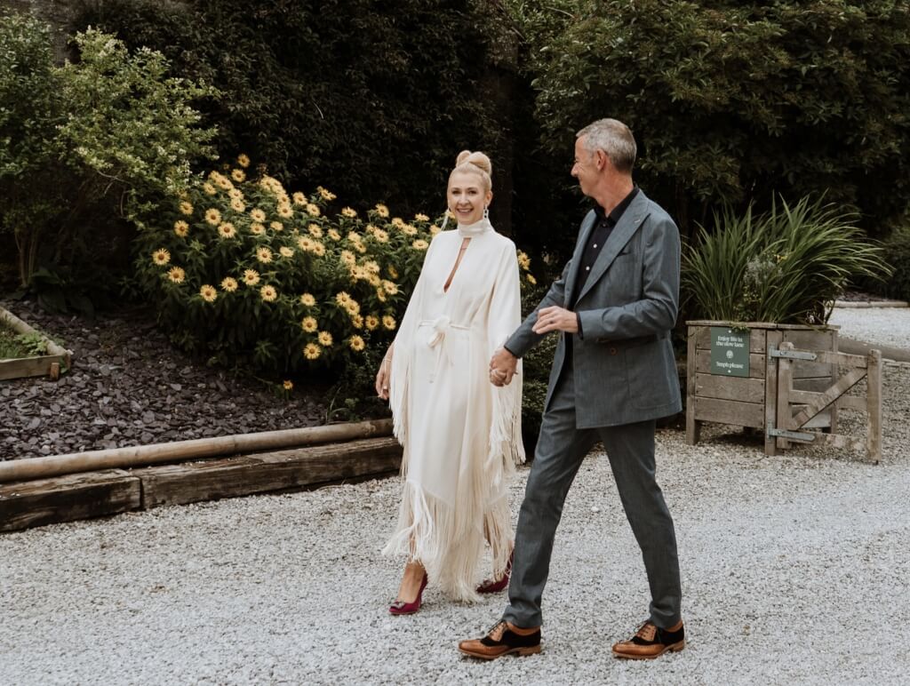 Married Couple On A Gravel Path Surrounded By Flowers