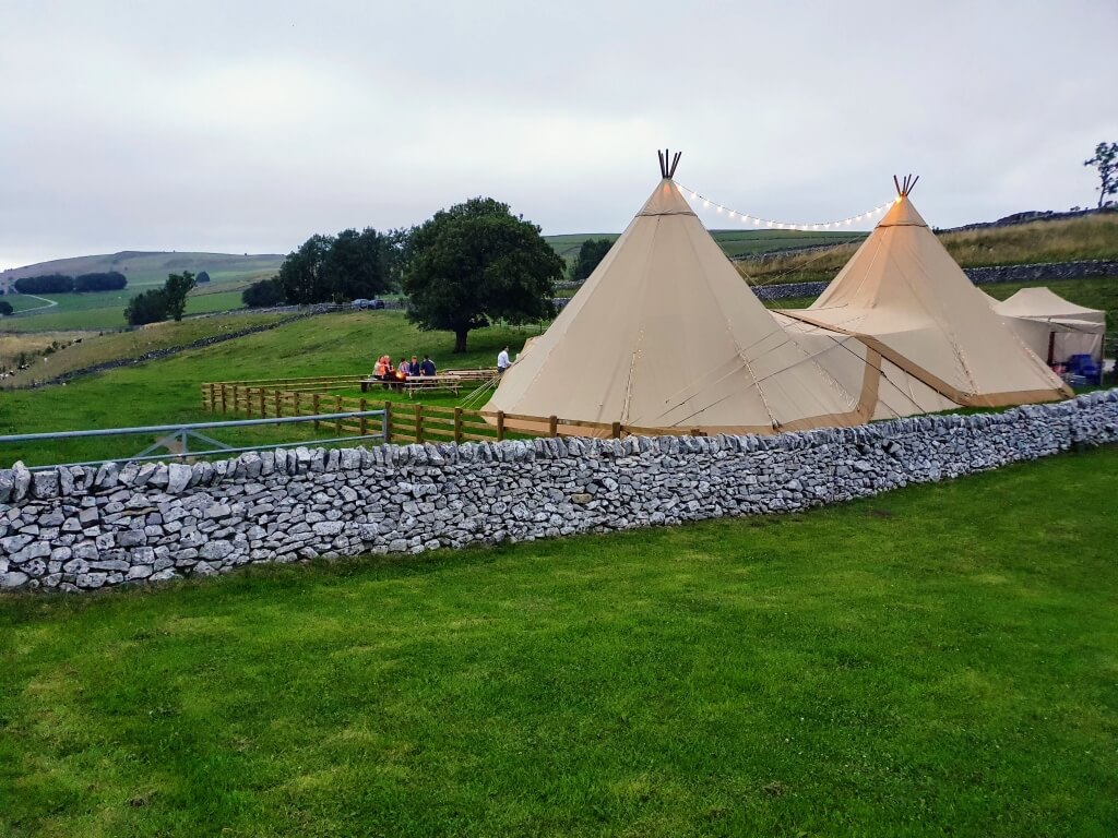 Tipi In A Field Next To A Stone Wall Overlooking A Valley